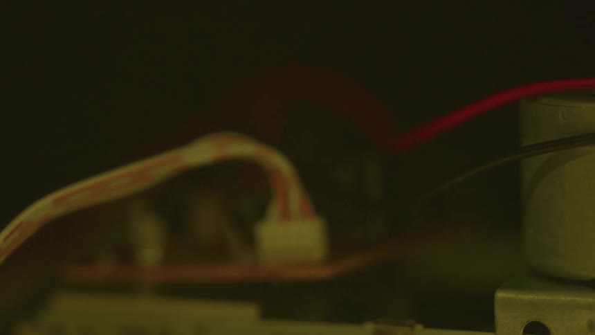 A close view of the inner electronics of a machine shows a circuit board with various colorful wires connected to it as the lights in the room slowly dim and go completely dark
