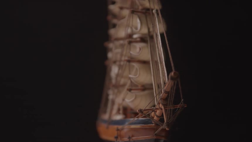 A detailed model ship with multiple sails and rigging is displayed against a dark background