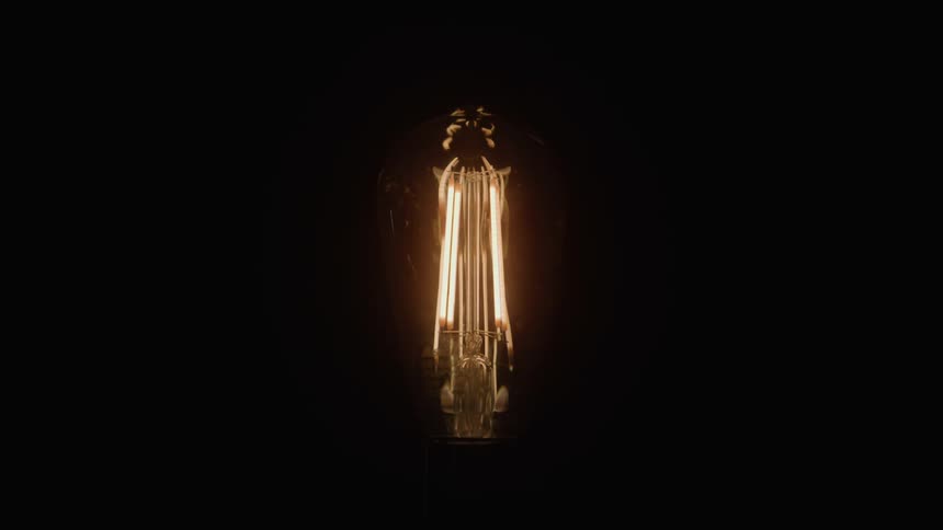 Lit incandescent bulb highlighting its filaments in the dark