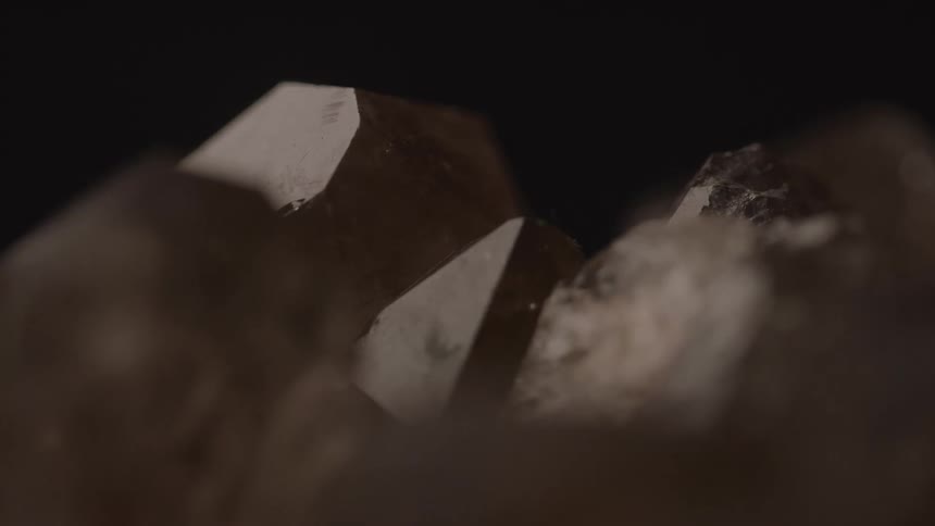 Brown crystals with faceted faces highlighted against a dark background