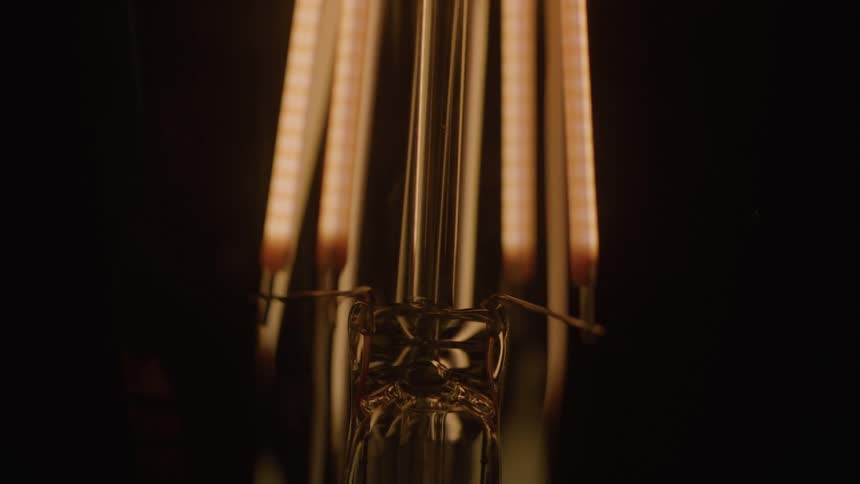 The glowing filaments of an incandescent light bulb gradually dim fading to darkness