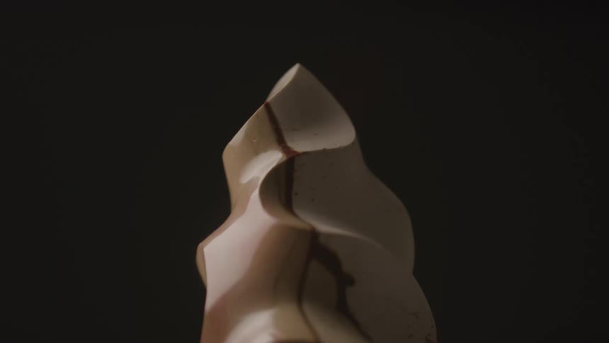 Pointed sculpture in light tones with brown veins set against a dark background