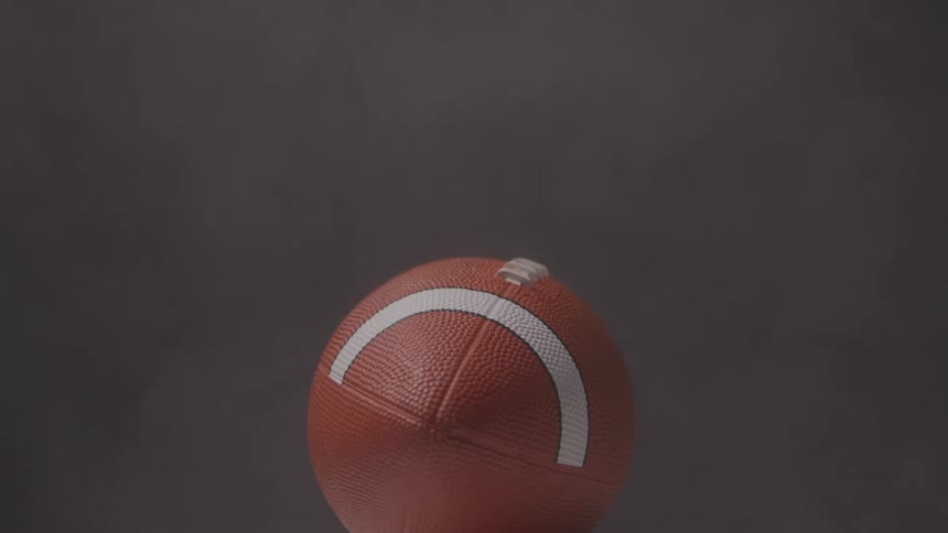 The video shows a football spinning in a slow upward motion against a dark background the camera is focused on the ball capturing the texture and white stripes as it rotates