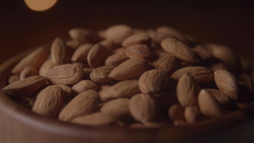 The video shows a wooden bowl filled with various nuts and seeds including whole almonds pecans and pumpkin seeds the camera focuses on the bowl and the nuts slowly rotate showing them in a closeup shot