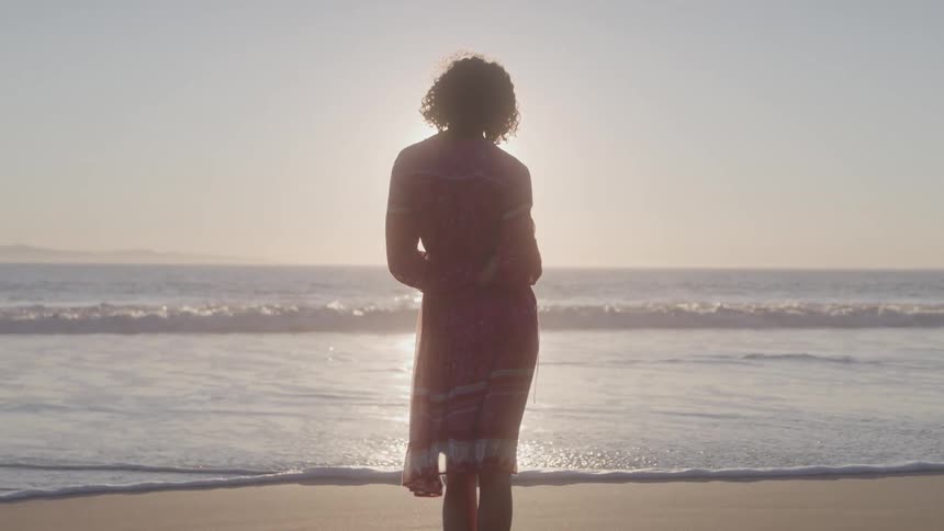 Woman in dress looking at the sun on the horizon on the beach