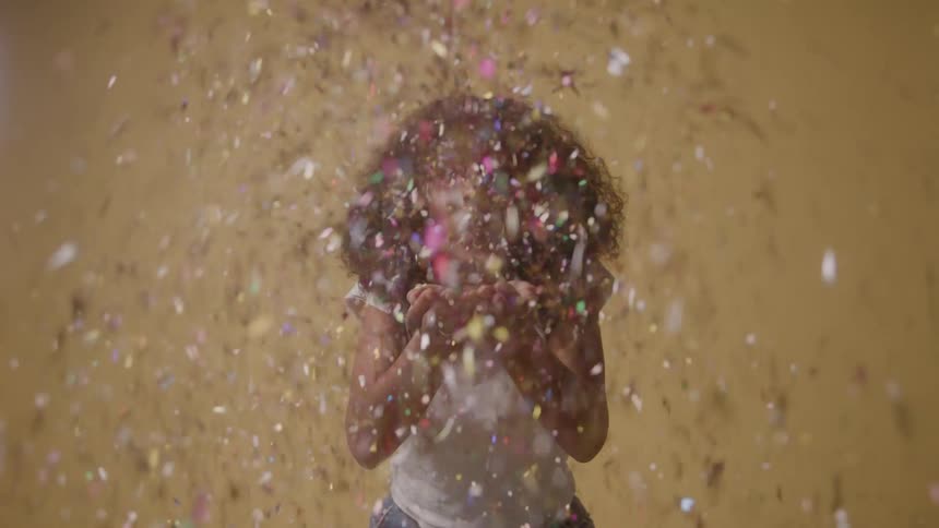 A woman smiles and blows glitter