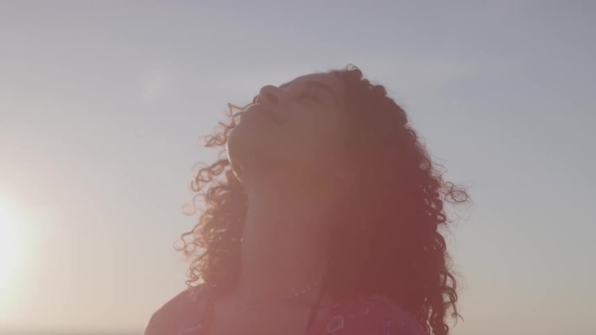 Curly haired woman with happy expression looking up outdoors