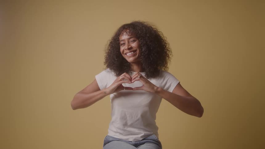 Smiling woman forms heart with hands toward camera