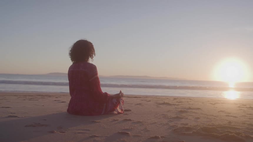 A woman is sitting on the sand on the beach
