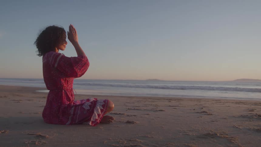 Woman sitting on the beach meditating with hands together