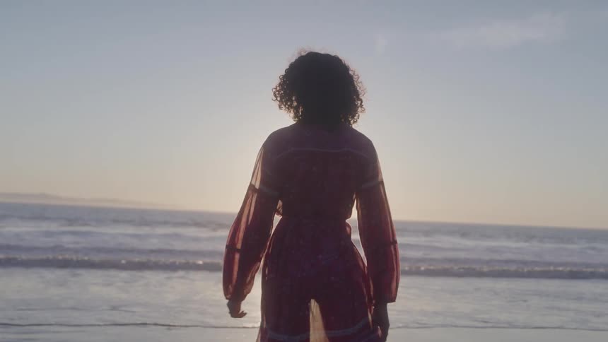 A woman is walking on the beach at sunrise