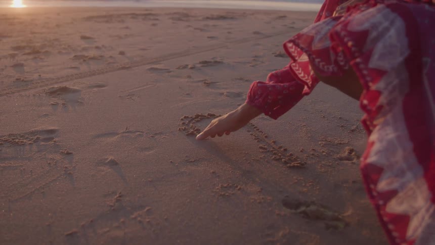 A woman traces a heart in the sand during the day