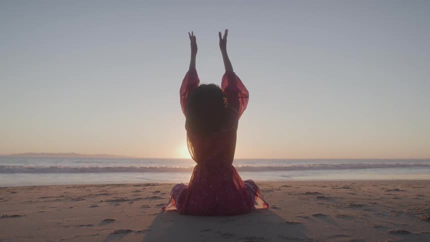 A woman sitting on the beach raises her arms