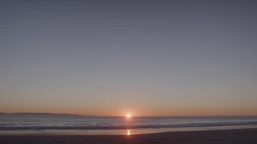 Sunrise casts a warm glow over the ocean and sandy beach
