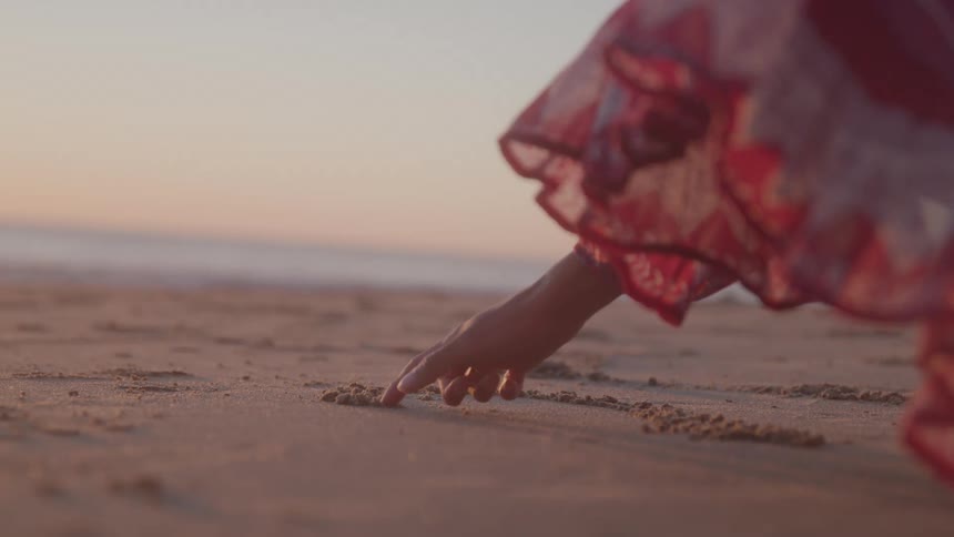 A woman drawing in the sand at the beach with her fingers