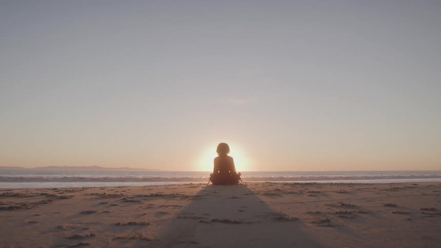 Person sits on the sand watching the sunrise over the sea