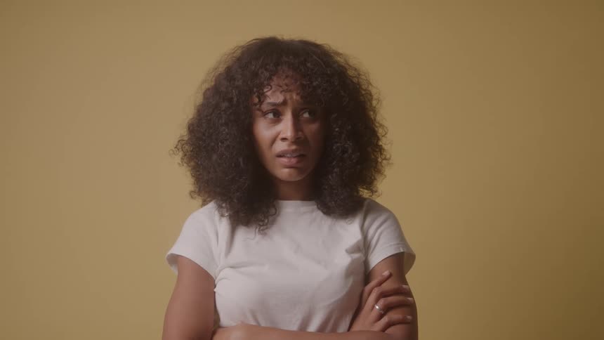 Woman with curly hair against a yellow background making faces