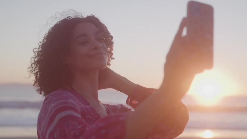 Woman with curly hair on the beach taking a selfie