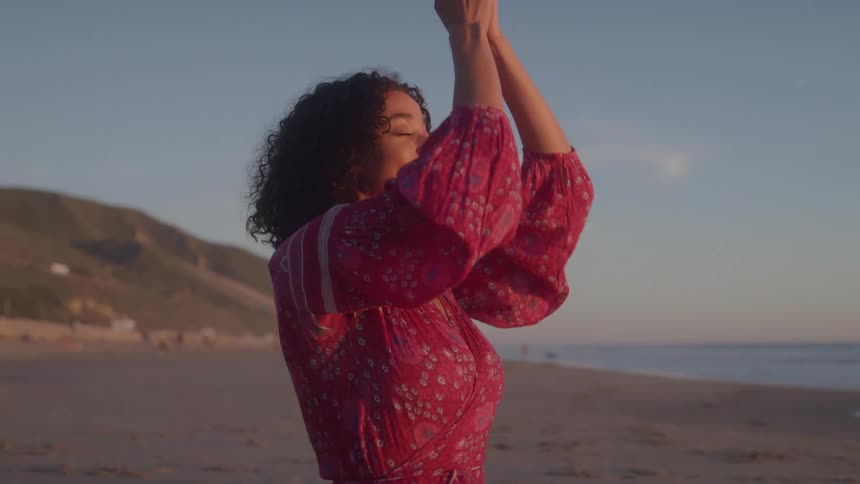 Curly haired woman in yoga pose on beach at sunrise