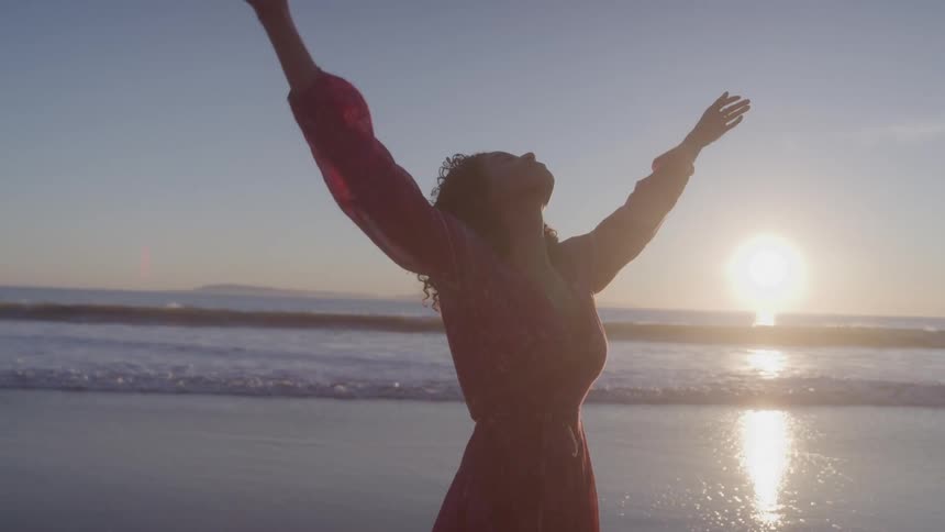 Woman spreading her arms while standing on the beach at dawn
