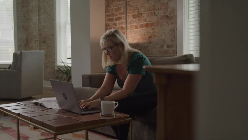 The woman is typing while sitting on her couch