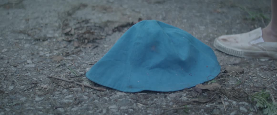 A person walks over and picks up a hat from the ground