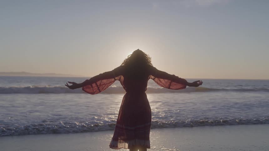 Woman in dress with open arms in front of the sea