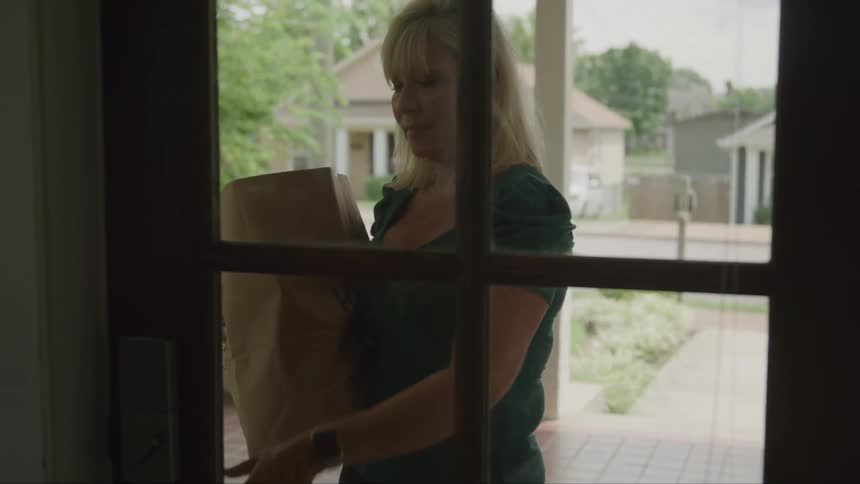 Woman entering the house carrying a brown paper package