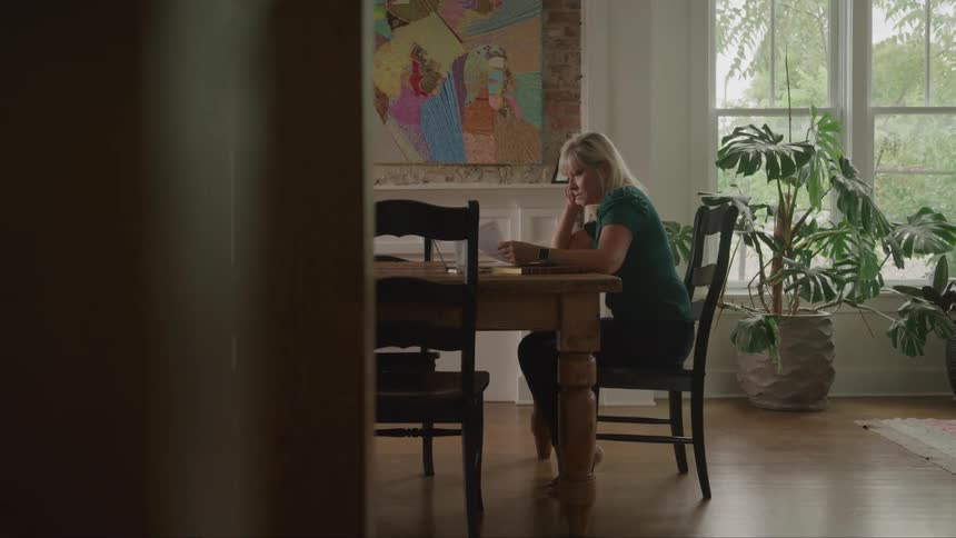 Woman sitting at a table resting her face on her hand while looking at an electronic device