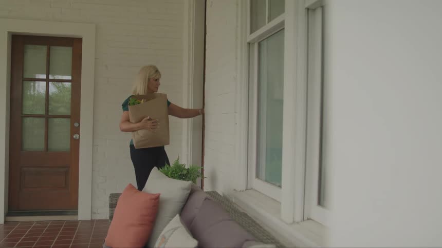 Woman carrying a paper bag with groceries while opening the door to her house