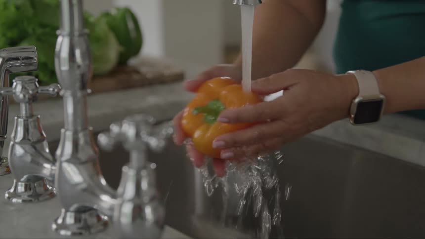 Woman washing yellow bell pepper over kitchen sink