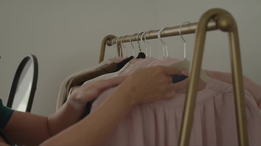 Hand selecting a pink blouse from a clothing rack