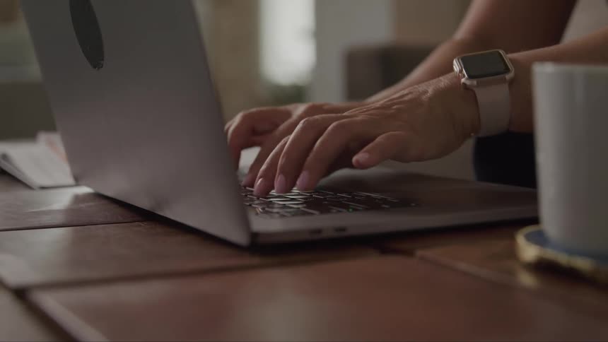 Close up of a woman typing on a laptop computer placed on a desk in a room during daytime
