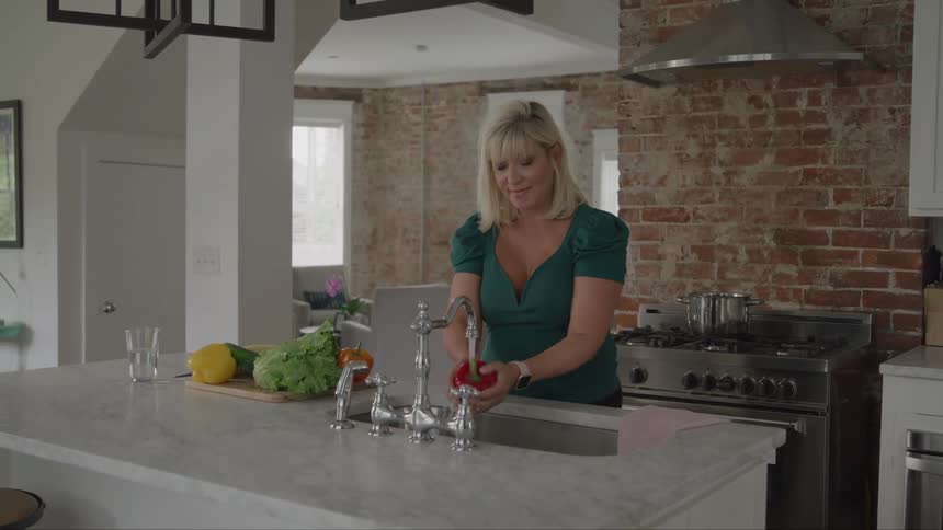 A woman washes vegetables in the sink and places them on a chopping board while standing in the kitchen during daytime