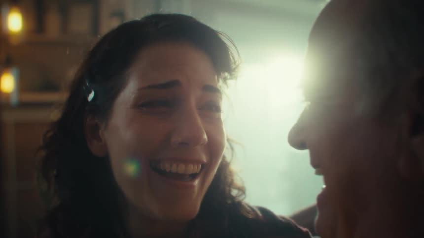 The video shows a closeup of a persons profile as they watch something offscreen the background is slightly out of focus with warmtoned lights glowing softly