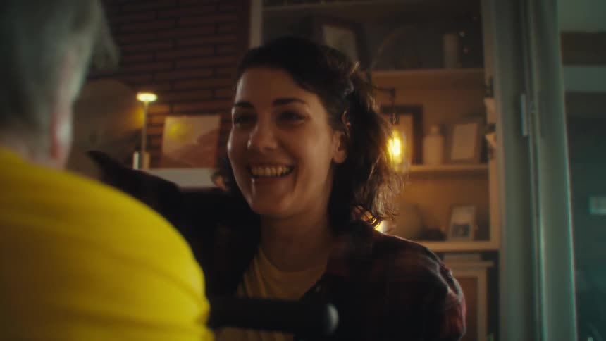 A woman with brown hair and a man with white hair sitting on a wheel chair celebrate excitedly as they both look at each other with happy expression and embrace