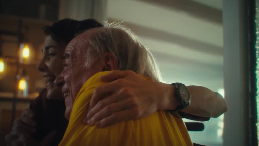 Close up of an elderly man and a young woman celebrating winning while watching tv in a living room during daytime
