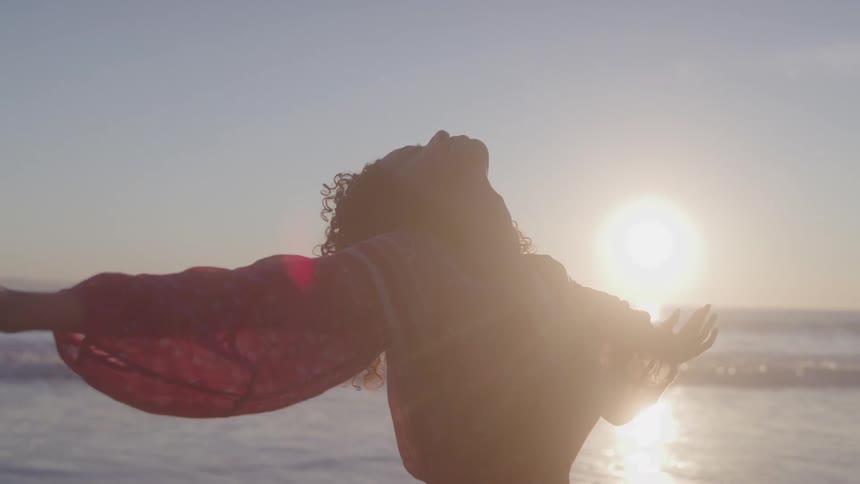Woman with arms wide open standing near the ocean at sunset