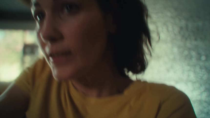 A close view shows a woman with dark hair wearing a yellow shirt who is laughing with an excited and happy expression as she plays video games