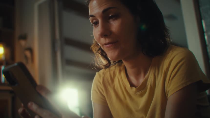 Woman holding a cellphone and looking at the screen with a slight smile