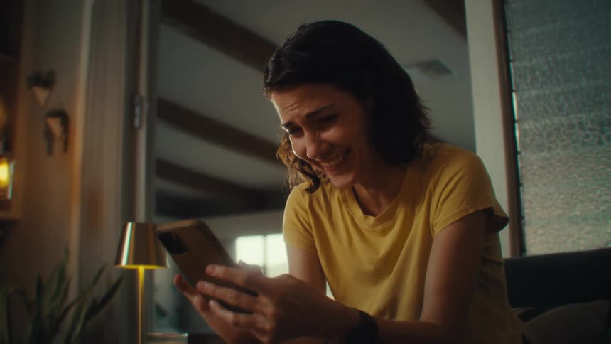 A woman inside her home using her phone and smiling