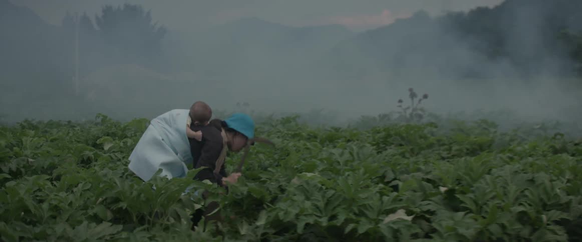 A woman carries a baby on her back as she works in a field