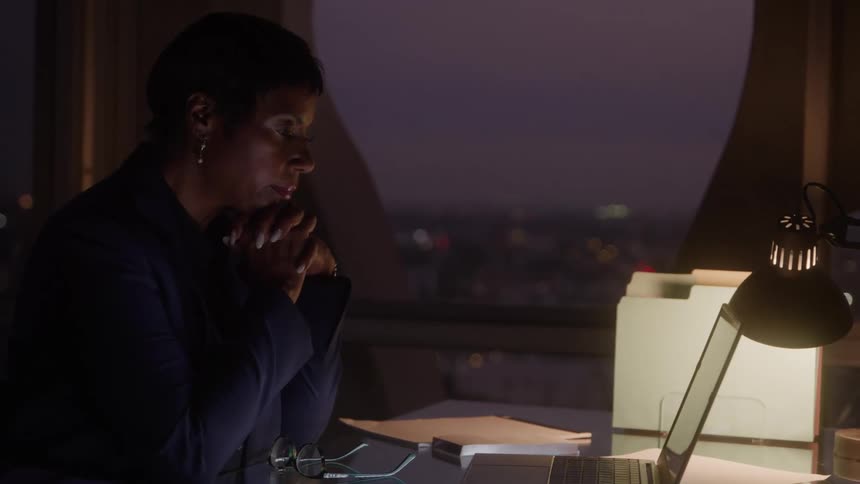 A woman is sitting at the office desk in front of her laptop