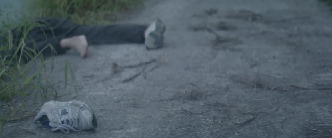 A person lays motionless with one shoe off on asphalt