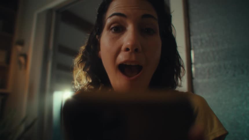 A woman raises a selfie stick and says hi into the camera