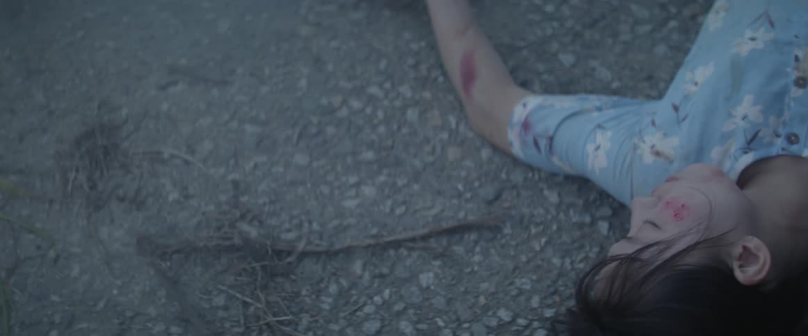 A bruised woman lays on the asphalt