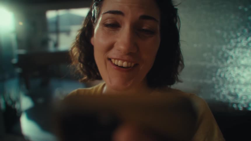 A young woman has a video call on her phone while in her living room talking excitedly to the caller
