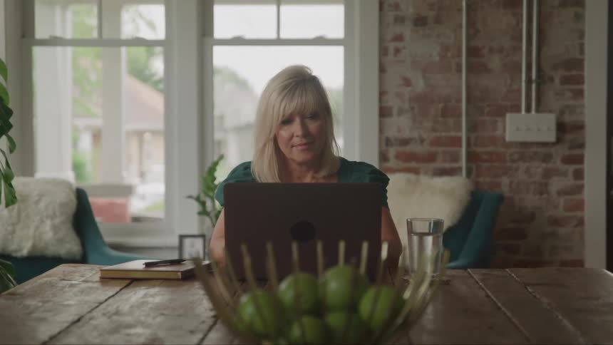 Woman using a laptop sitting at a table with fruits and a glass of water