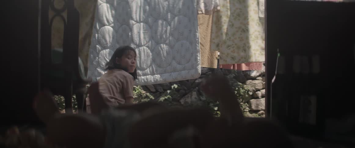 A woman is crouched in a yard looking back at a baby behind