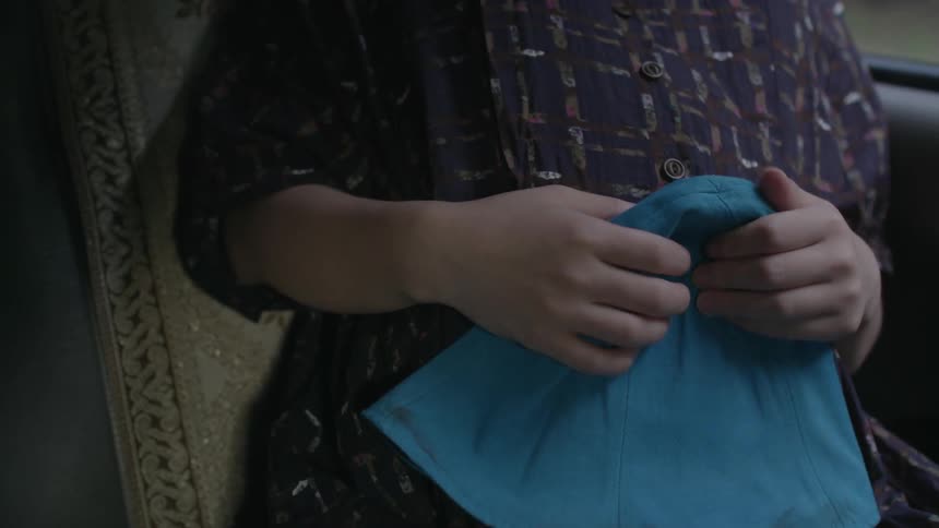 A pregnant woman sits in a vehicle holding a blue cloth